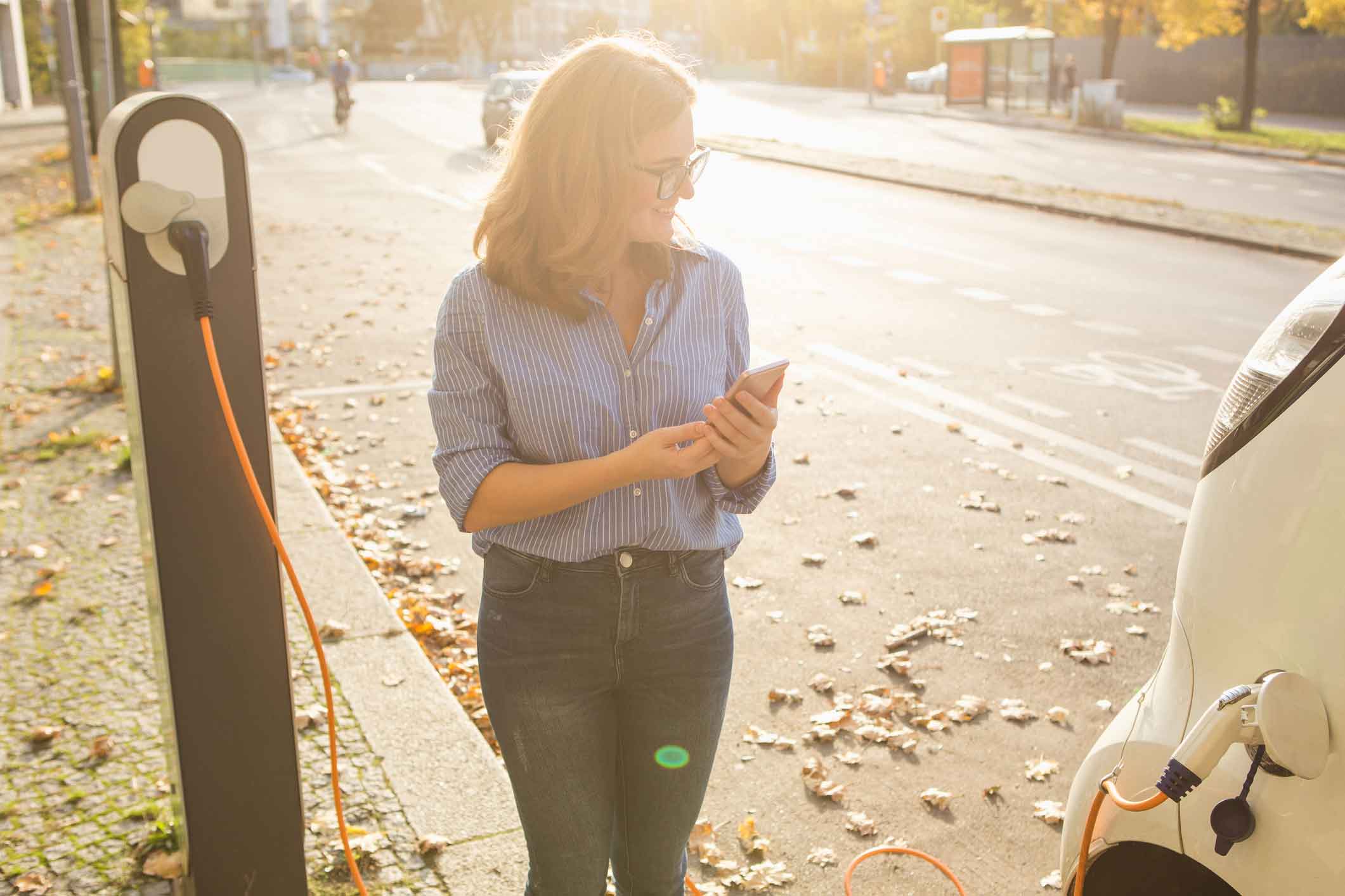 ev-benefits-(web) woman with phone looking at electric vehicle